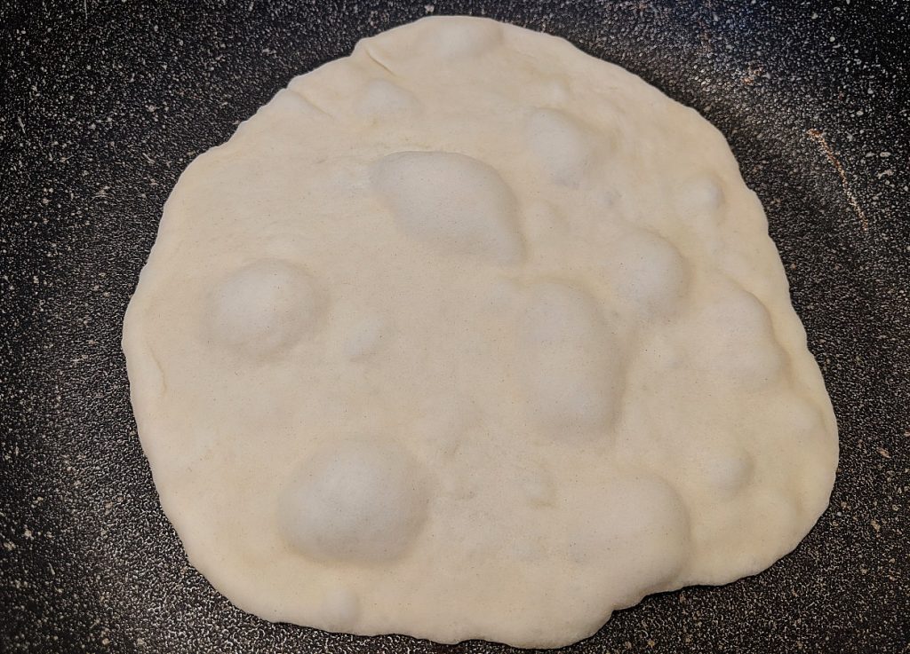 Flattened tortilla dough in plan with bubbles forming