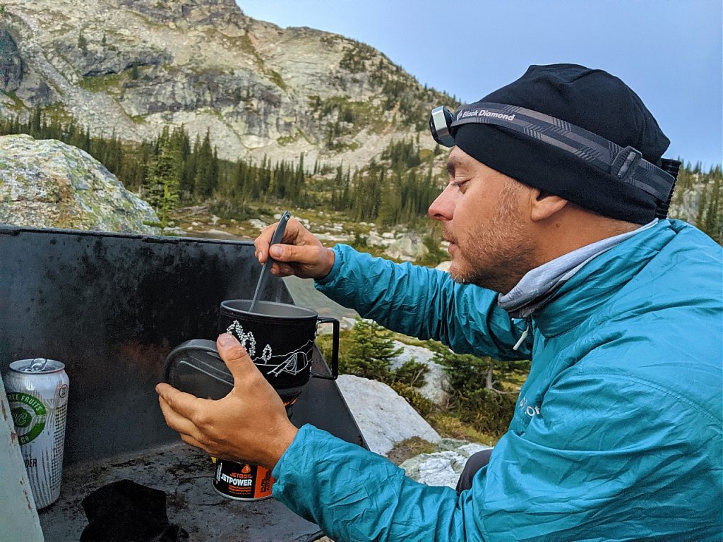 JR looking at contents of backpacking stove post with mountainous backdrop