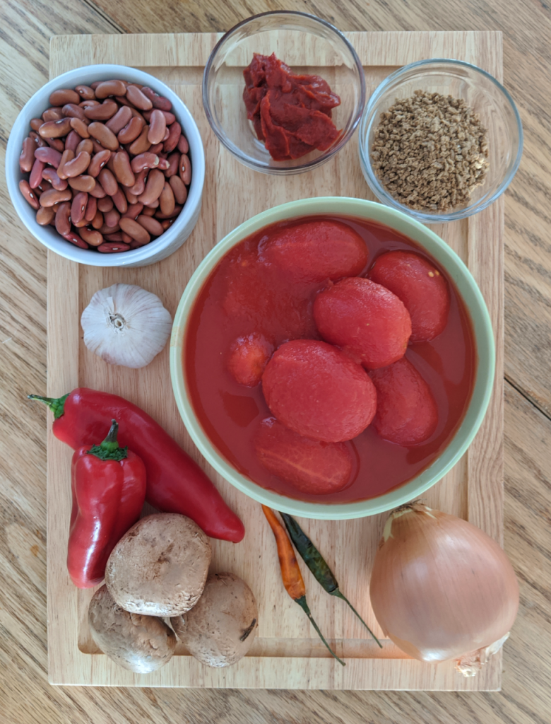 Ingredients for chili sin carne on chopping board - mushrooms, chilis, onions, beans, garlic, tomatoes, textured vegetable protein