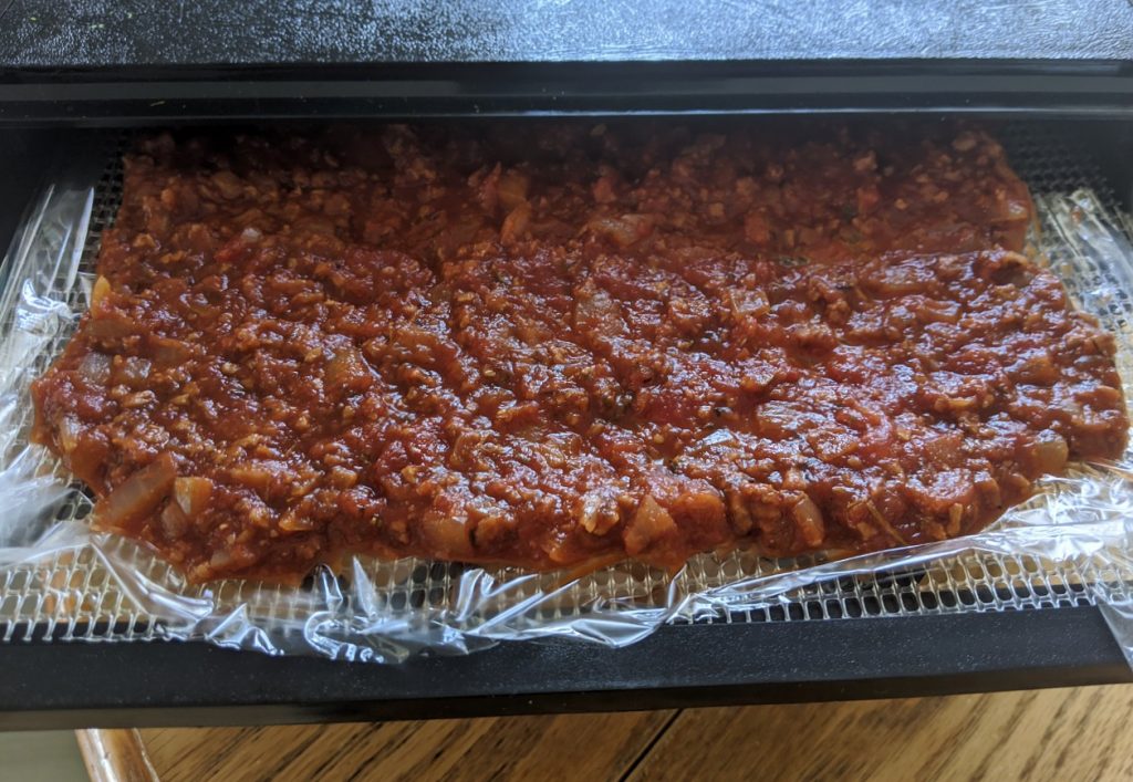 Dehydrator tray covered with wax paper and veggie bolognese sauce, ready to dehydrate